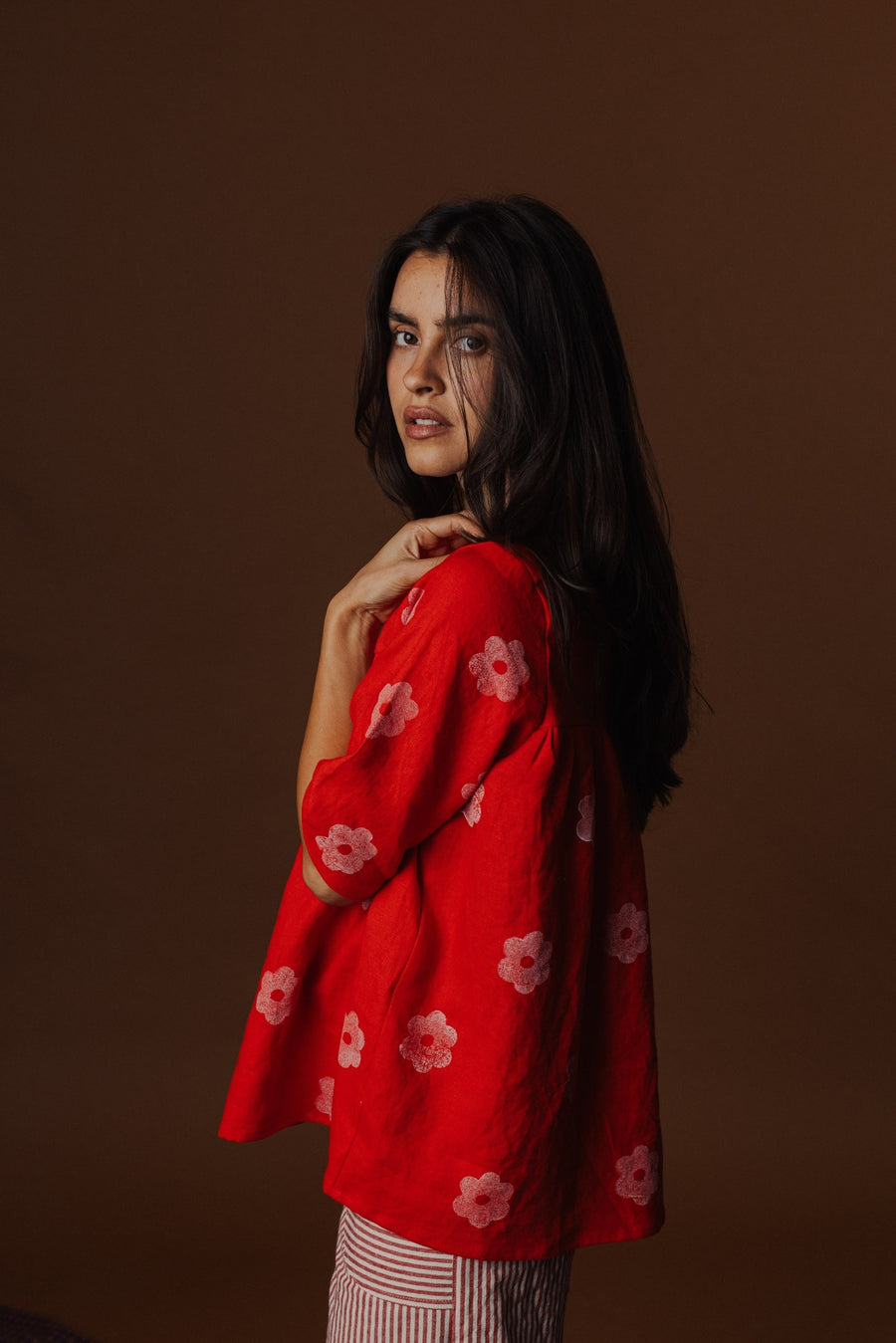 Over-the-shoulder portrait highlighting the relaxed sleeve structure and floral block print of the red linen blouse.