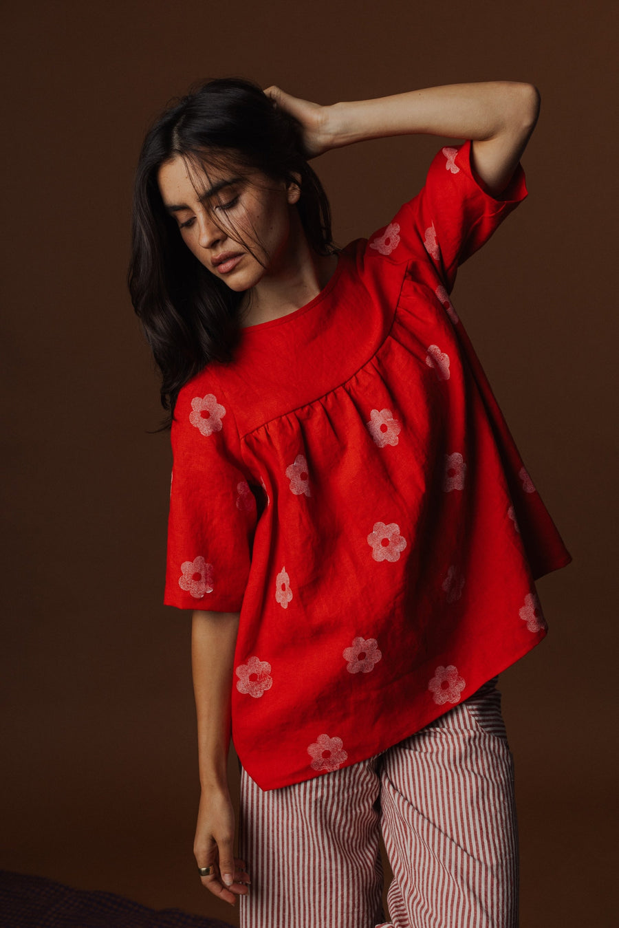 Studio portrait of model Briana wearing the red hand block printed Pamut Apparel Claire Linen Blouse in size XS paired with red and white striped trousers.