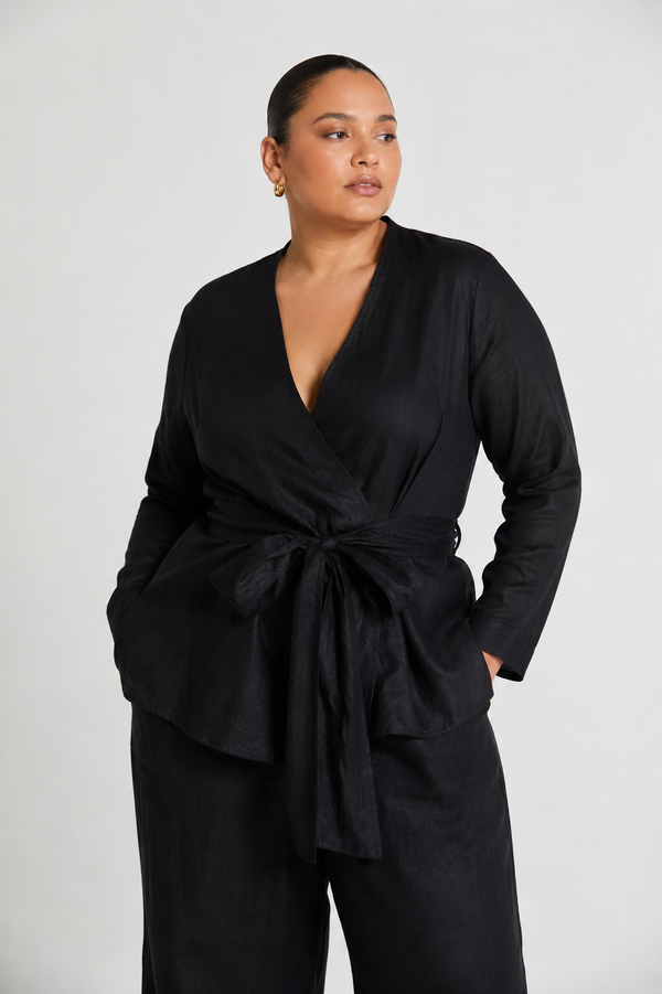 A plus-size model wearing the reistor Power Moves Shirt in Black, highlighting a size-inclusive, structured fit with a cinched tie-front waist, V-neck, and long sleeves against a white background.