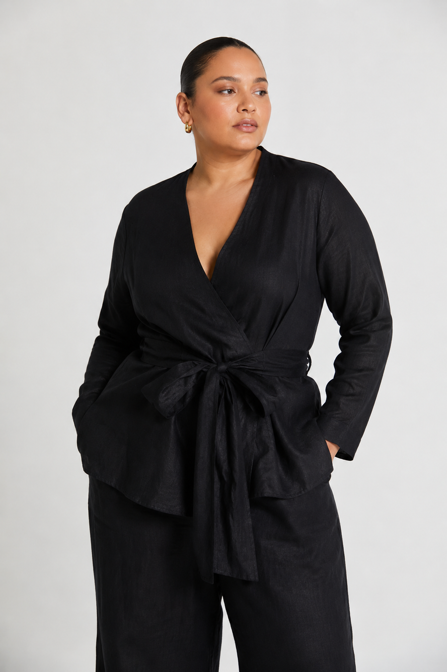 A plus-size model wearing the reistor Power Moves Shirt in Black, highlighting a size-inclusive, structured fit with a cinched tie-front waist, V-neck, and long sleeves against a white background.