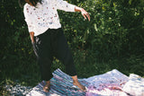 Model posing outdoors on an outdoor rug surrounded by greenery, wearing the white splattered ScrapShirt and black tapered pants