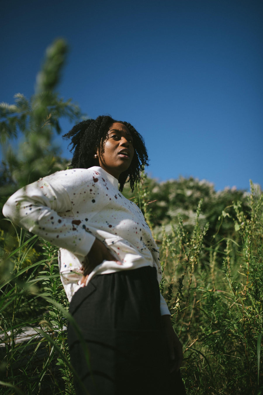 Back view showing the standing collar and oversized fit of the ScrapShirt pullover worn outdoors among tall green grass under a clear blue sky
