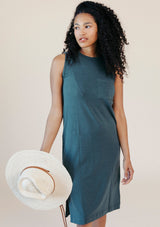 Studio portrait of model wearing the size-inclusive Poplinen Sophie Tank Jersey Dress in Pine green holding a woven sun hat.