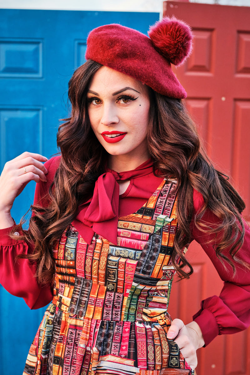 Close-up portrait of model wearing the Retrolicious novelty book print dress with a scoop neck layered over a red long-sleeve bow tie blouse.