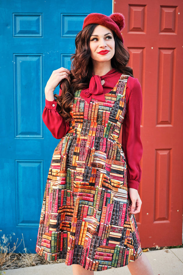 Model wearing the Retrolicious Don't Judge a Book by Its Cover book print fit and flare dress styled over a burgundy bow top with a red beret.