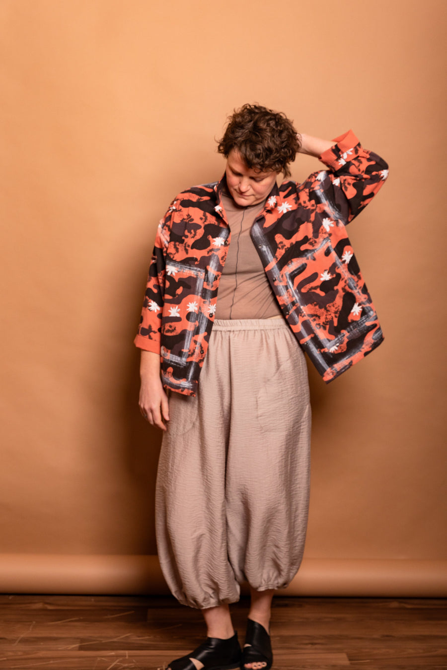 Front view of the model adjusting the popped collar on the Sherbet orange hand-outlined Studio Jacket.