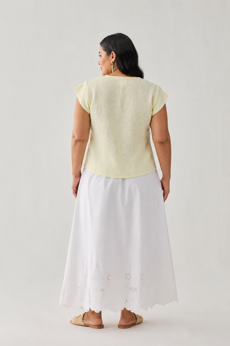 Full back view of a mid-size model showcasing the clean, regular-fit shoulder construction and cap sleeves of the pastel yellow linen top, paired with a long white cotton skirt.
