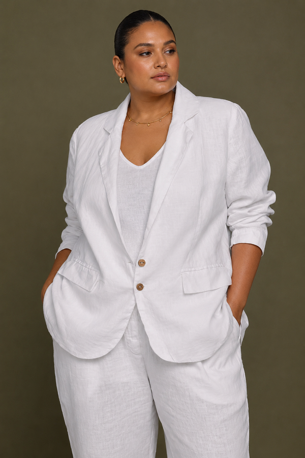 Front view of a plus-size model wearing the Reistor She's Everything Blazer in White, showcasing the regular fit, notched collar, and sustainable wood-look button closures with hands in pockets.
