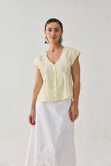 Front view of a model styled in the pale yellow linen V-neck blouse, showing its relaxed yet gently fitted waist silhouette over a white summer skirt.