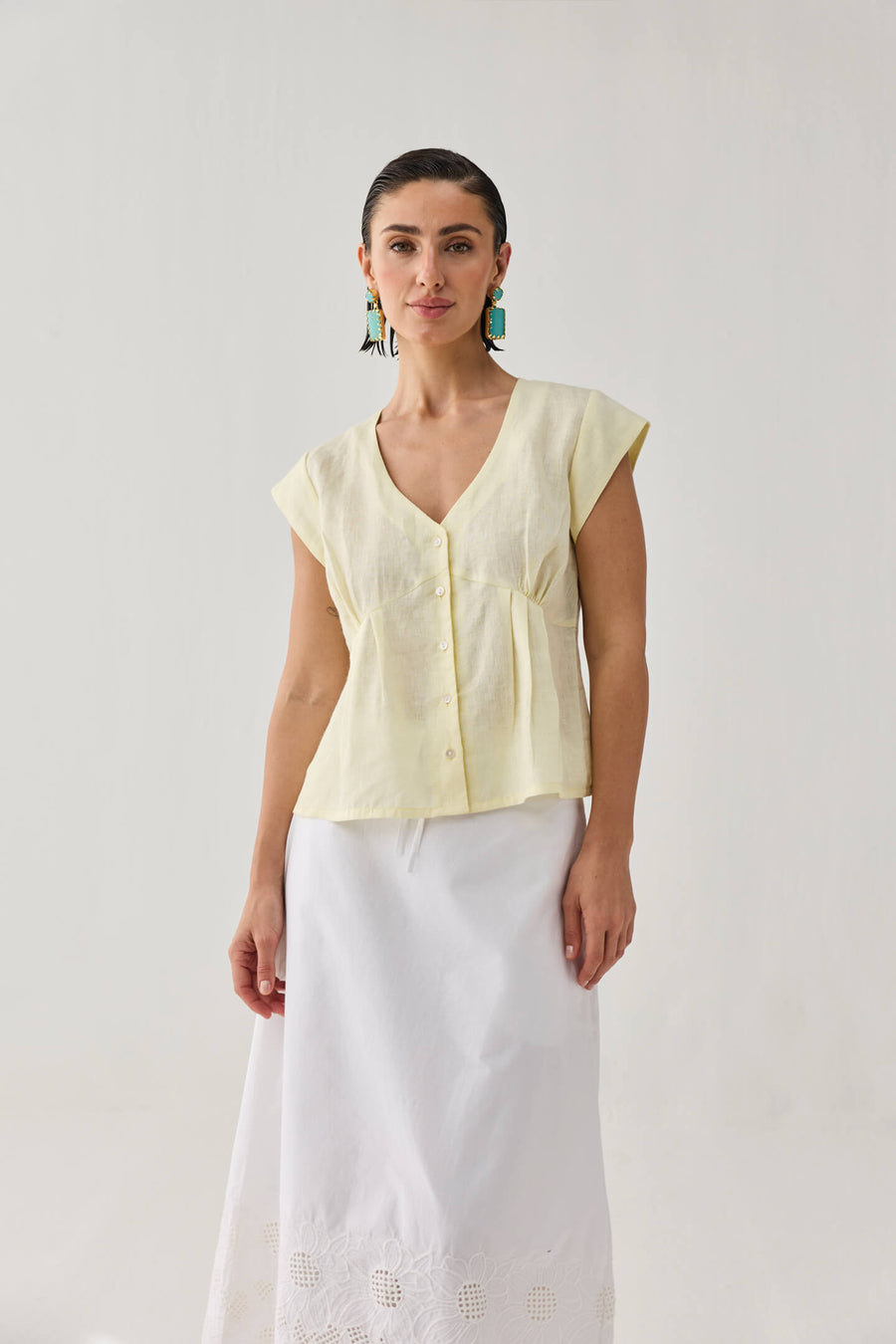 Front view of a model styled in the pale yellow linen V-neck blouse, showing its relaxed yet gently fitted waist silhouette over a white summer skirt.