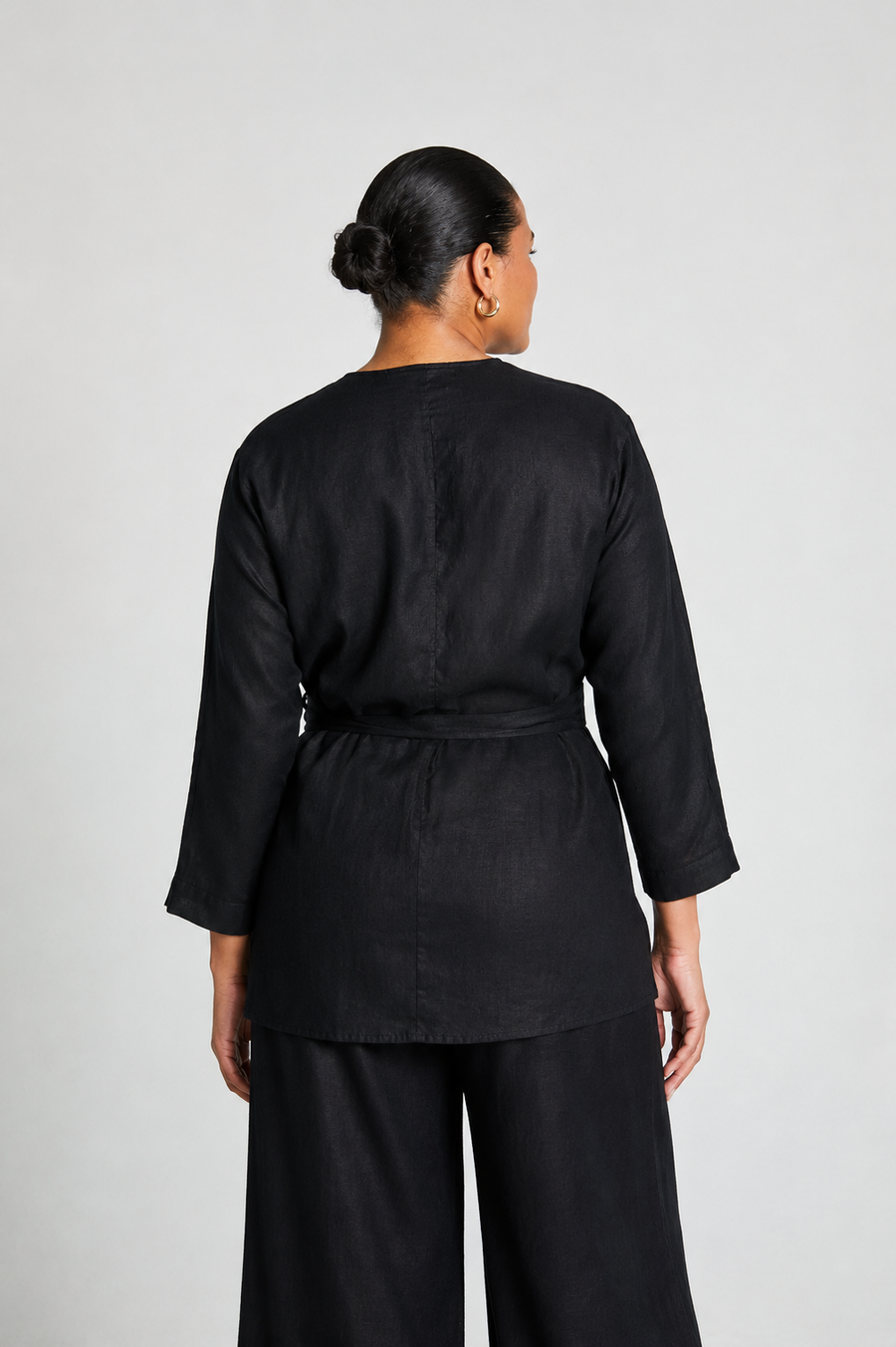Back profile of the 100% hemp black wrap shirt by reistor, featuring a clean tailored seam down the back and a cinched tie waist. Styled on a plus-size model for an inclusive-size fit presentation.