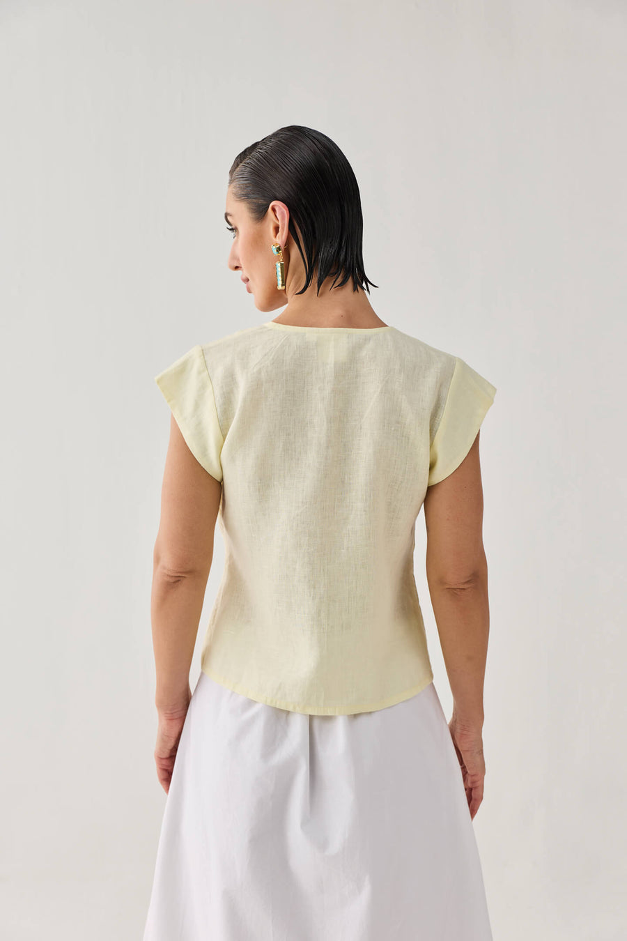 Back profile angle of a model wearing the Butter Lemon linen top, highlighting how the short cap sleeves cleanly frame the shoulders.