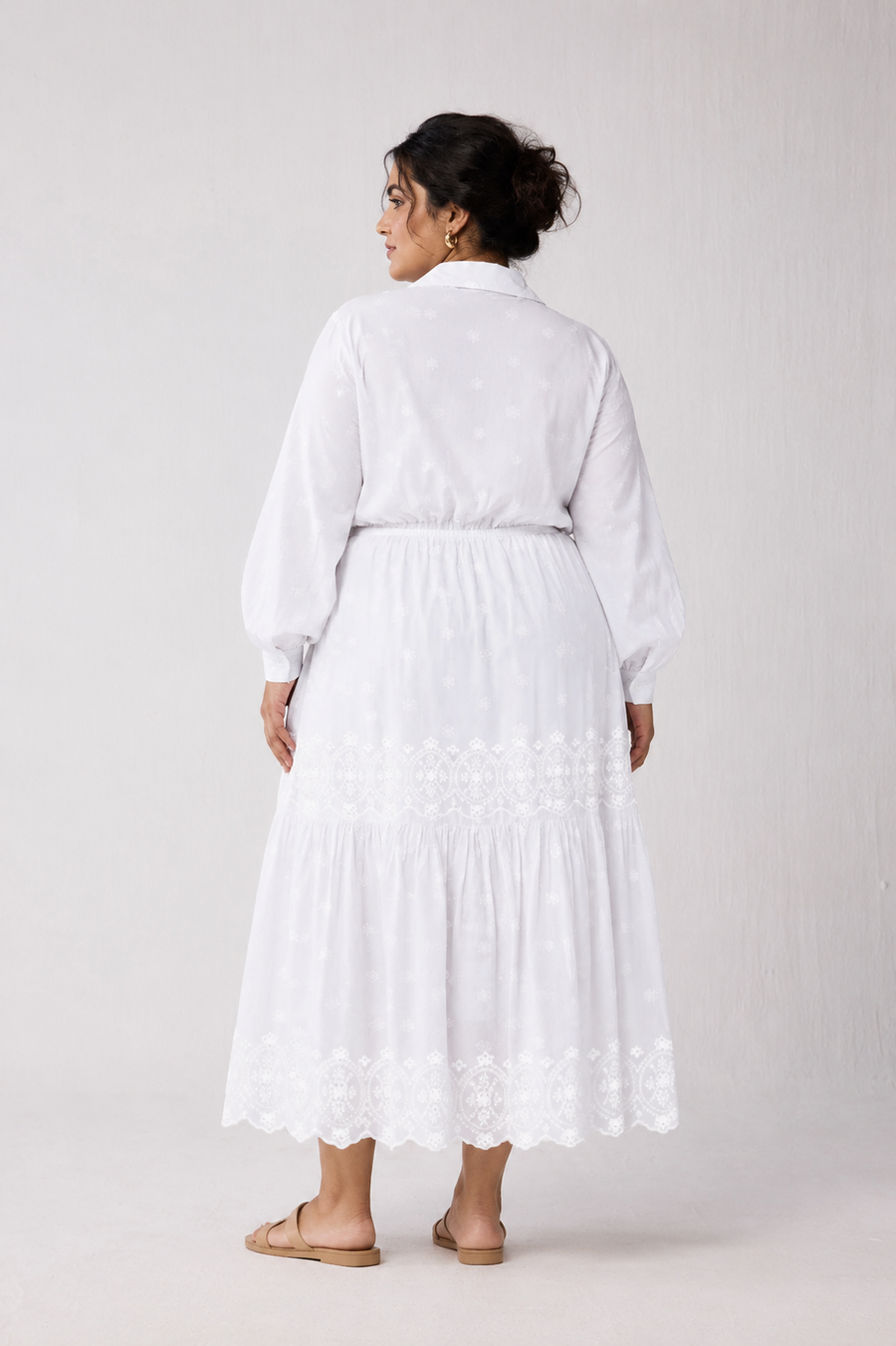 Full back view of a plus-size model with an updo hairstyle wearing the white tiered maxi dress, showcasing the elasticated drawstring waistline and detailed embroidery band along the skirt.