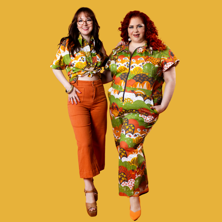 Studio portrait of two models showcasing the Blue Platypus Meadow Print collection in jumpsuit and top styles against a yellow background.