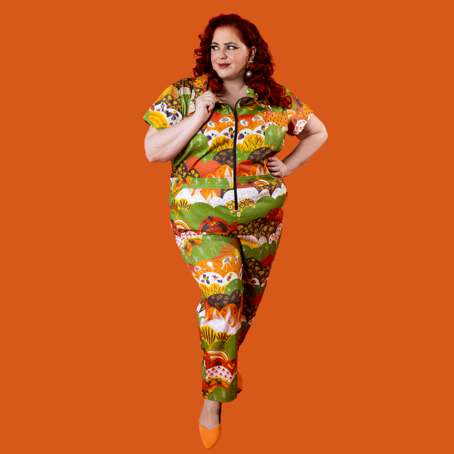 Full-length front view of a model posing with a hand on her waist wearing the Blue Platypus Earth-toned Meadow Print cotton stretch jumpsuit.