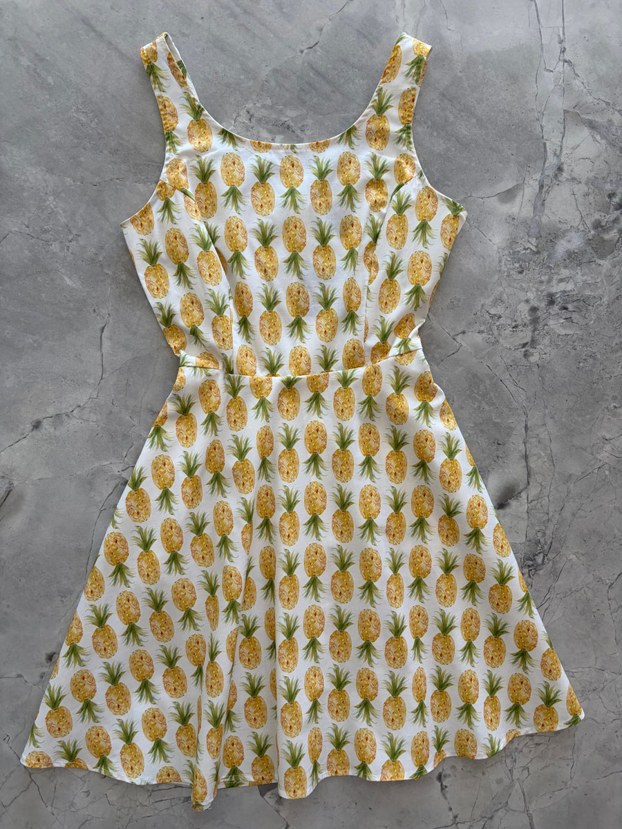 Flat lay product photo of the Retrolicious Pineapple Skater Dress on a gray marble background showing the full A-line skirt and scoop neck.