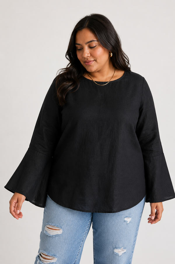 Front view of a plus-size model wearing Reistor's The Button Back Shirt in Black. The 100% hemp blouse features a regular fit, an elegant boat neckline, and prominent flared bell sleeves, styled casually with light-wash ripped jeans.