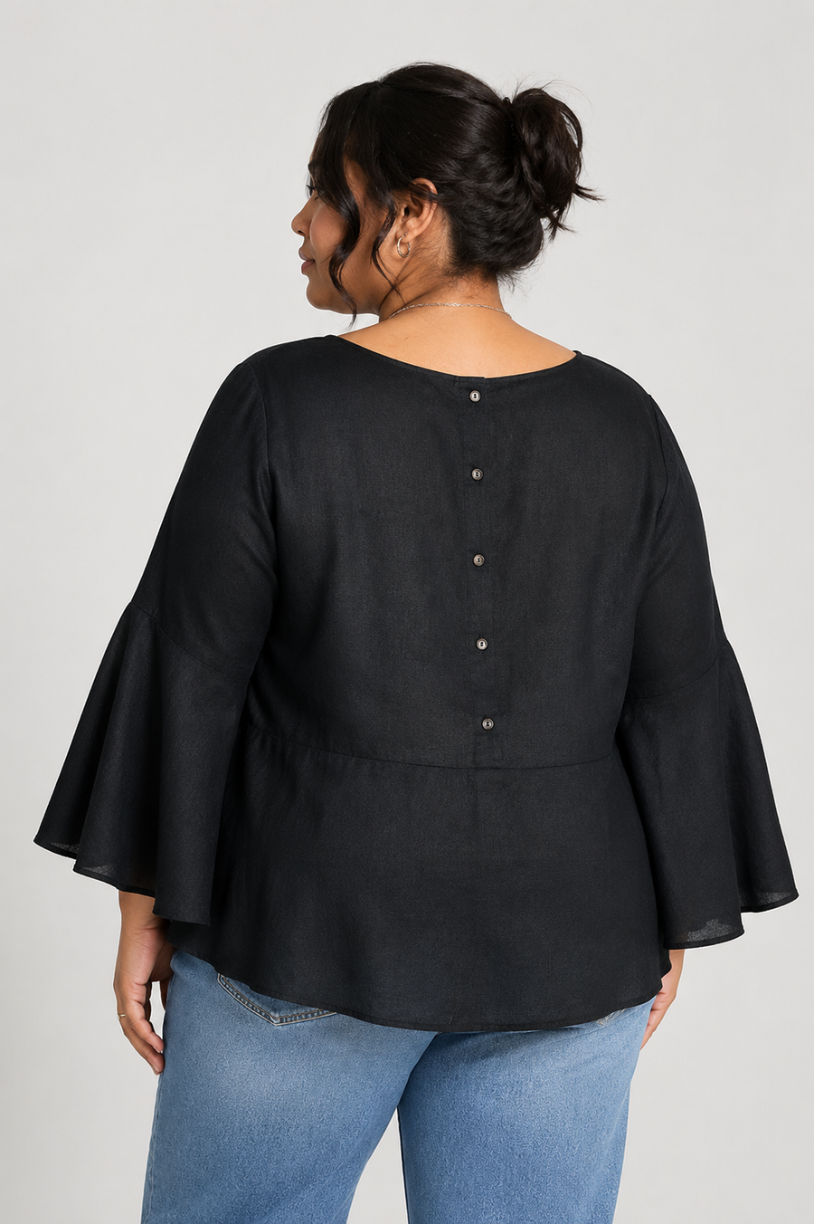 Back view of a plus-size model with her hair in a bun, highlighting the classic vertical back button placket detailing and refined waist line of the black Reistor shirt.