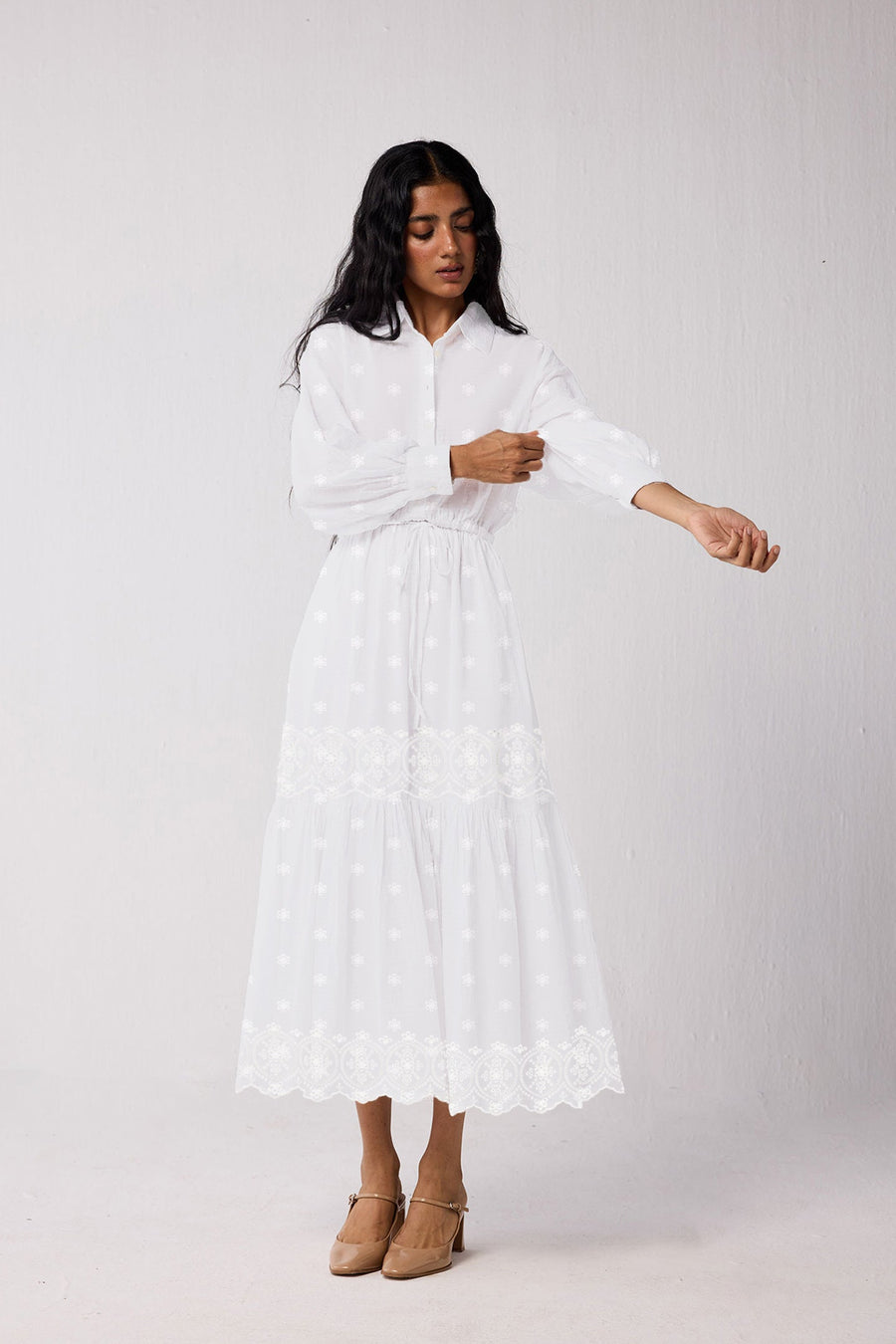 Full front view of a model rolling up the cuffed bishop sleeves of the white tiered maxi dress, highlighting its breathable, lightweight organic cotton composition.