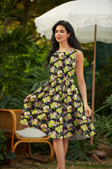 Full-length photo of a brunette model posing outdoors under a patio umbrella wearing the Retrolicious Wine Vintage Dress featuring a wine bottle and grape pattern.
