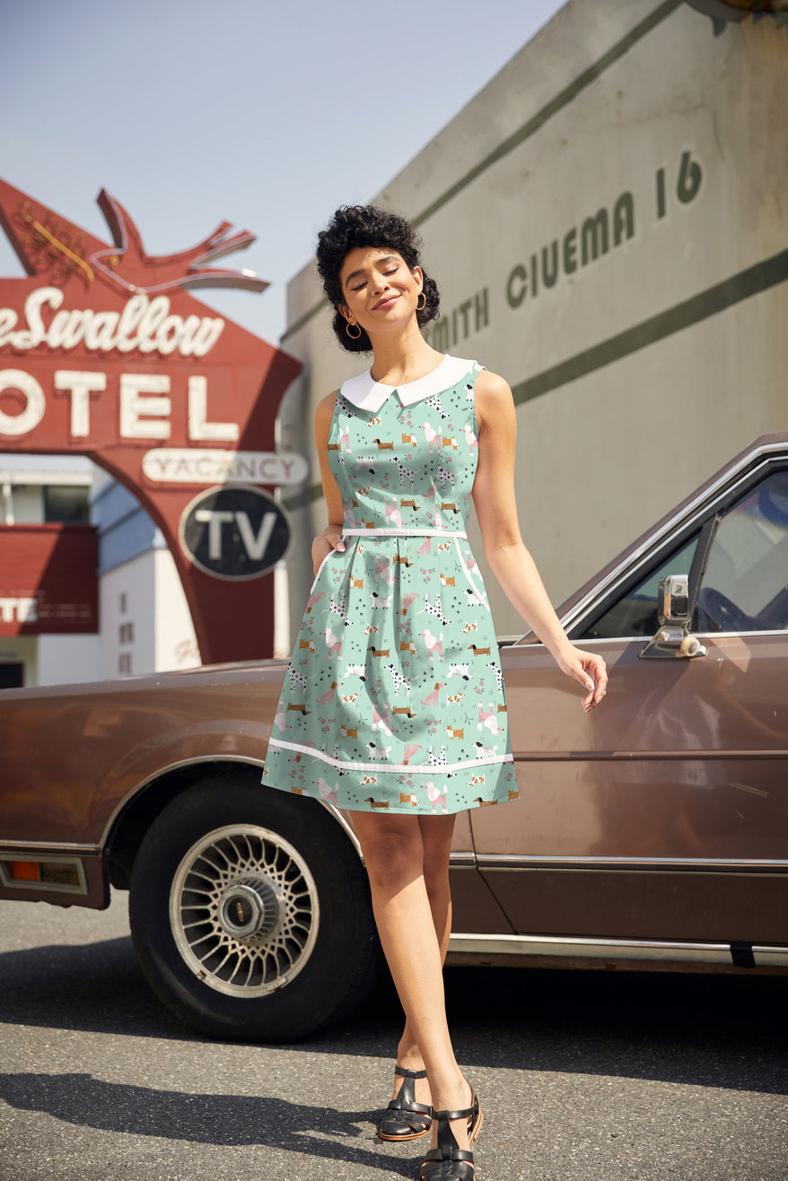 Full-length shot of a model wearing the Retrolicious mint green 1960s style dog print dress with a white Peter Pan collar and side pockets.