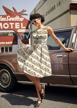 Model posing near a vintage car holding out the skirt of the Retrolicious Elizabeth Dress in Woodland Sunset print featuring piping and decorative buttons.
