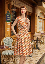 Medium shot of a redhead model styled in retro victory rolls posing outside a French bakery in the Retrolicious Cotton Candy Greta Dress.