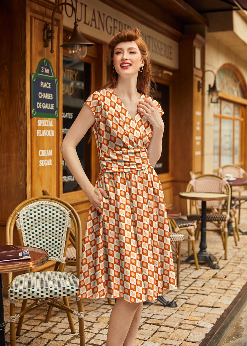 Medium shot of a redhead model styled in retro victory rolls posing outside a French bakery in the Retrolicious Cotton Candy Greta Dress.