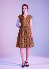 Studio portrait of a model wearing the Retrolicious Pumpkins & Flowers Greta Dress featuring a surplice V-neck and cummerbund waist.