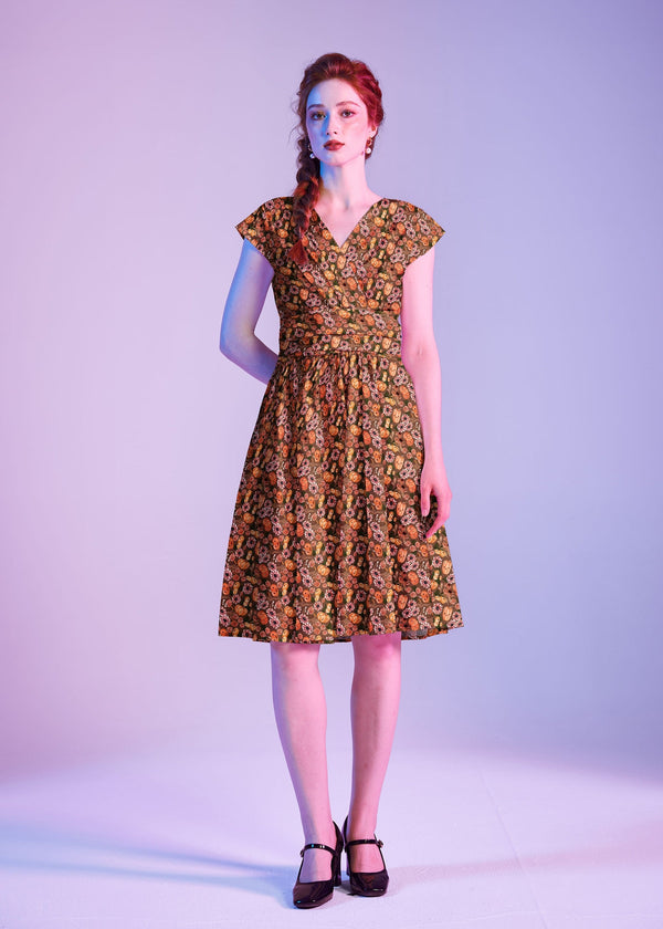 Studio portrait of a model wearing the Retrolicious Pumpkins & Flowers Greta Dress featuring a surplice V-neck and cummerbund waist.