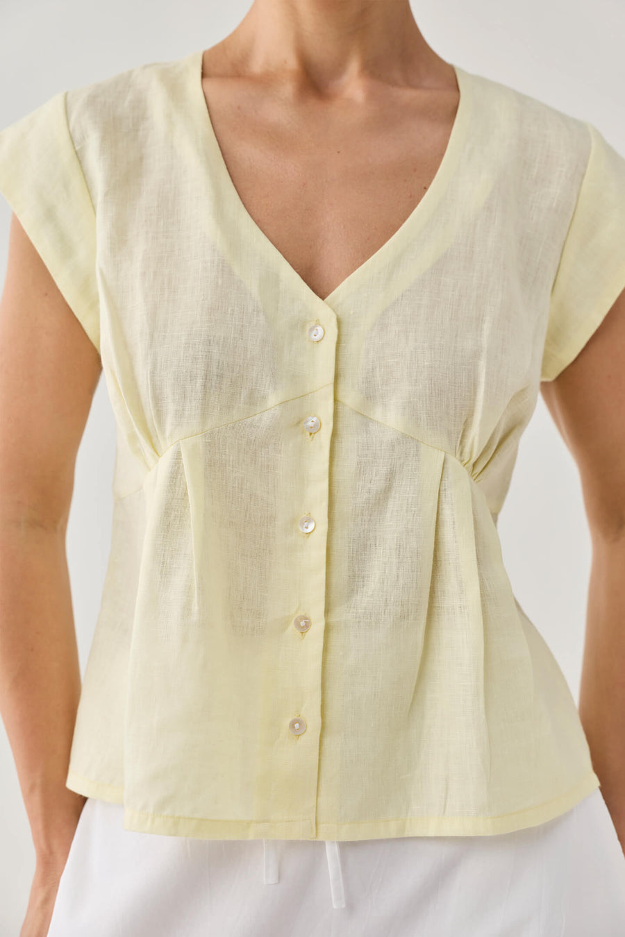 Close-up torso view of a model wearing Reistor's Deep V Neck Top in Butter Lemon, highlighting the button-down front, soft fabric gathering under the chest seam, and breathable 100% linen weave.
