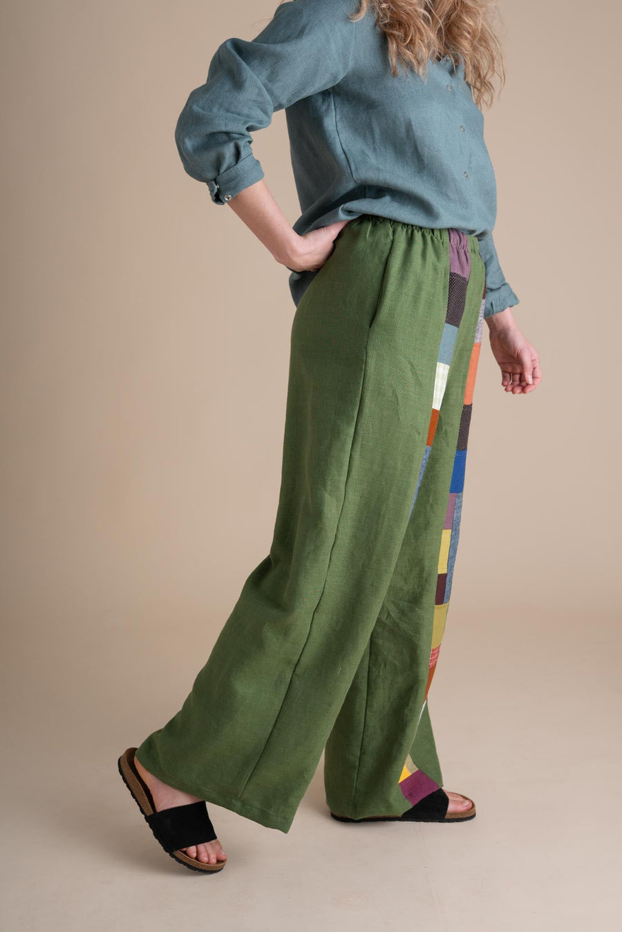 Side profile view of a model stepping forward in the relaxed-fit green linen Joystripe Pants by Conscious Clothing.