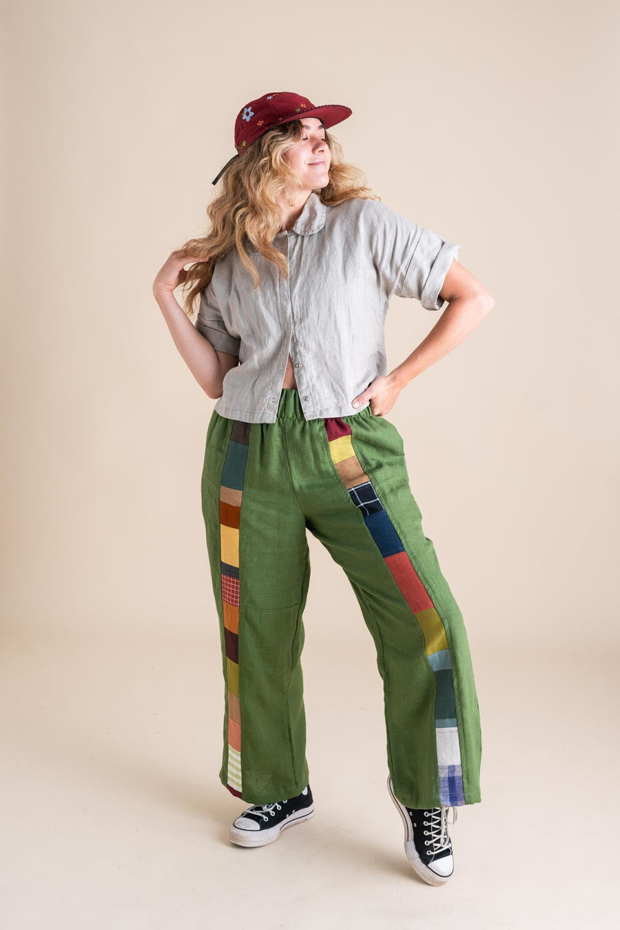 Full-length view of a model styling the clover green flax linen Joystripe Pants with black high-top sneakers, a grey short-sleeve top, and a red cap.