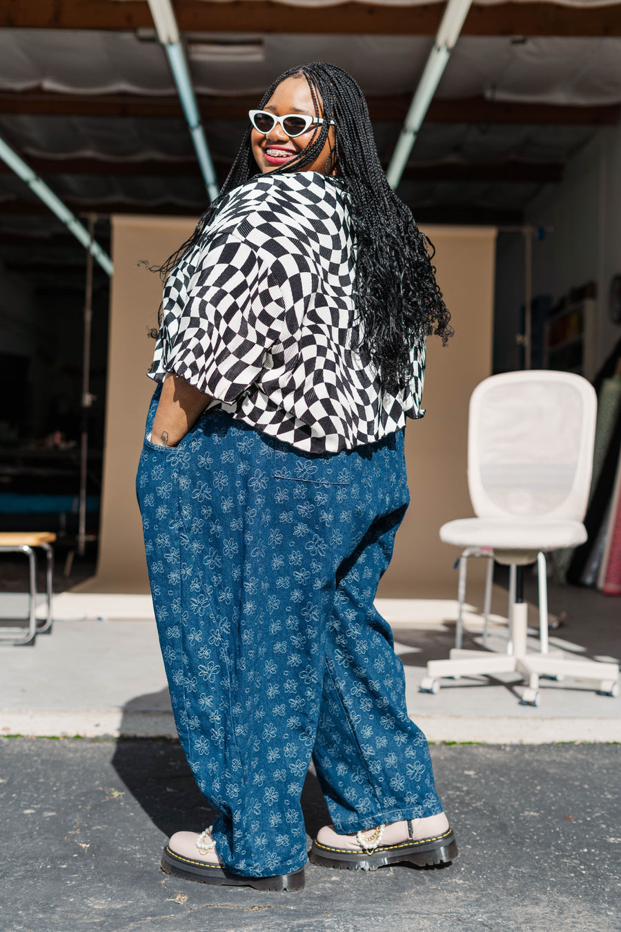 Back view of model Keda wearing the black and white wiggly checker Dizzy Favorite Tee paired with blue floral patterned pants.   