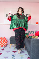 Full-length view of a model posing in the metallic green tinsel mushroom top, red undershirt, and black floral wide-leg pants.