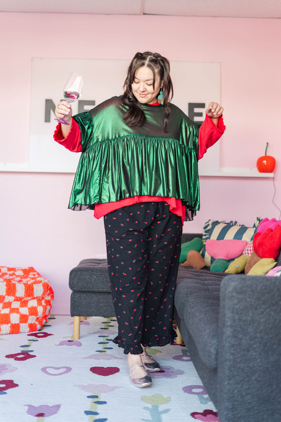 Full-length view of a model posing in the metallic green tinsel mushroom top, red undershirt, and black floral wide-leg pants.