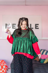 Model smiling while holding a glass, wearing the metallic Green Tinsel Mushroom Top layered over a red long-sleeve top.