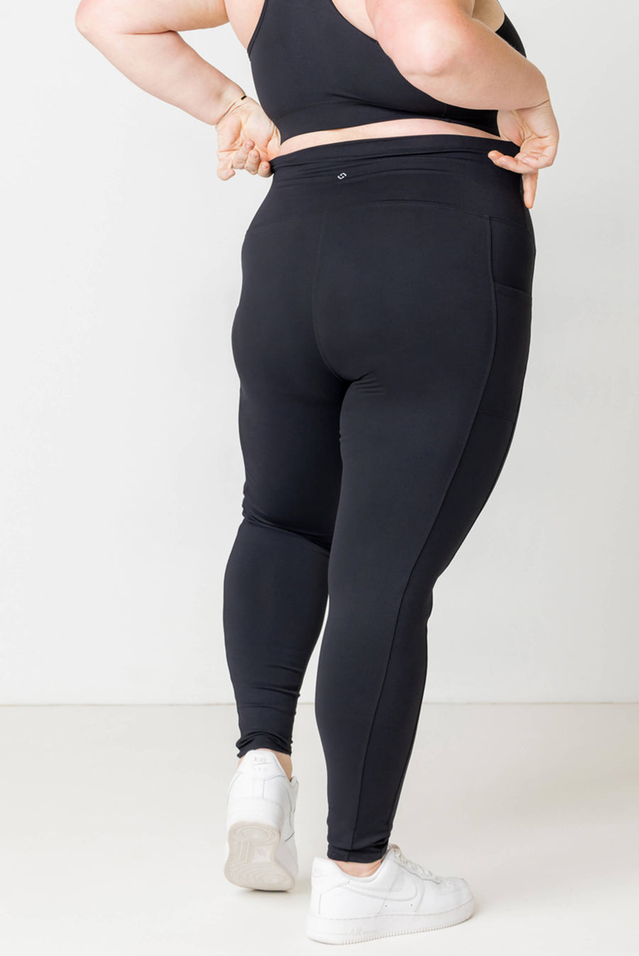 Back view close-up of a model wearing high-waisted black Superfit Hero compression ankle leggings, showing the stay-put waistband.