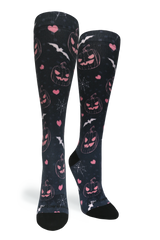 Studio portrait shot of a pair of Jill-O-Lantern knee-high compression socks featuring pink jack-o'-lanterns, hearts, bats, and spiderwebs on black fabric