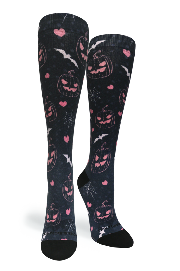 Studio portrait shot of a pair of Jill-O-Lantern knee-high compression socks featuring pink jack-o'-lanterns, hearts, bats, and spiderwebs on black fabric