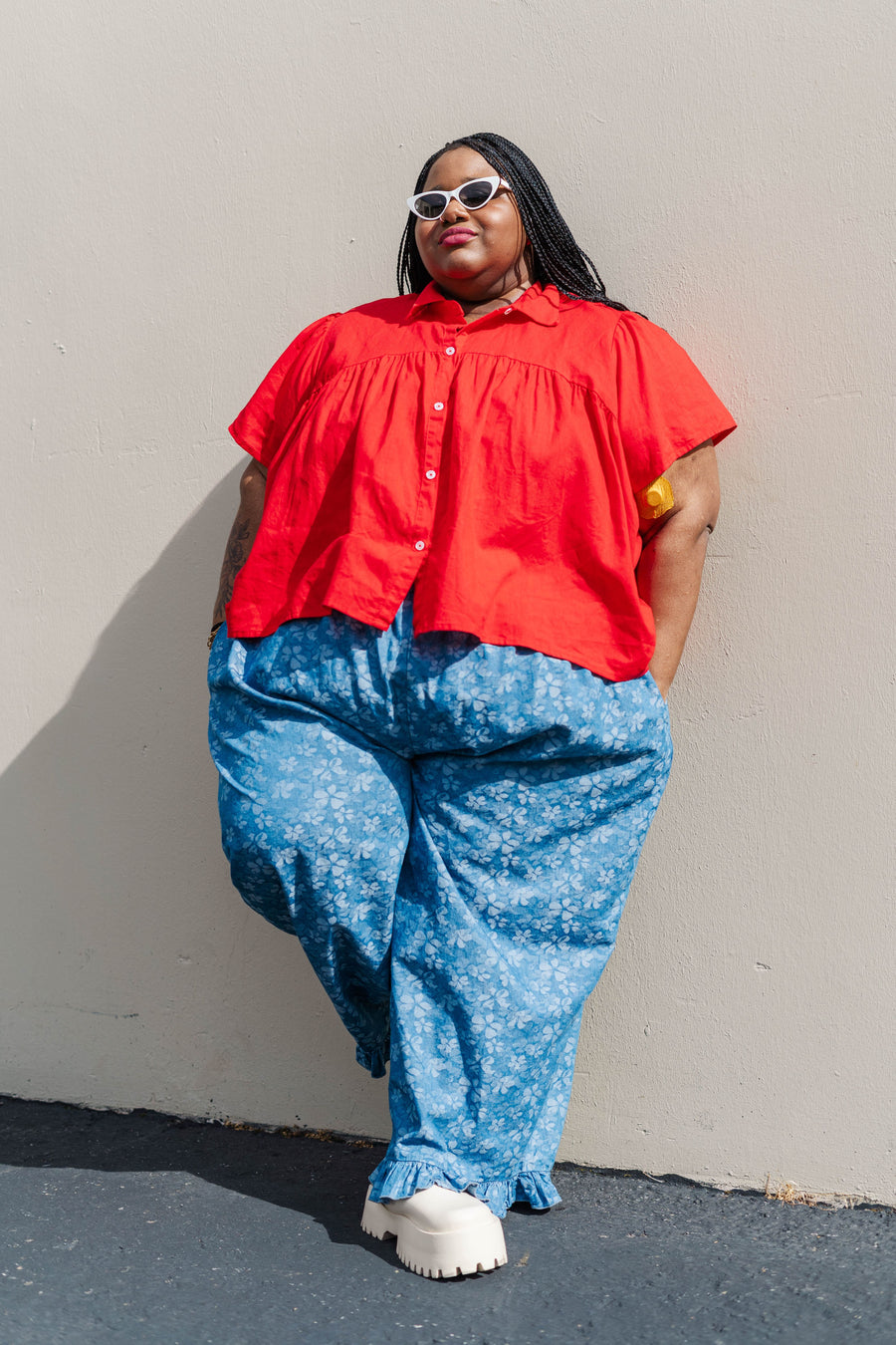 Outdoor full-length shot of model Keda leaning against a wall in the light floral chambray ruffle pants.