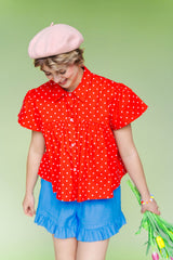 Mid-shot of a model looking down while wearing the Nettle Studios Cherry Polka Dot Button Mushroom Top, showcasing the voluminous, slightly cropped swing shape. Styled with bright blue shorts for a playful, size-inclusive fashion look.