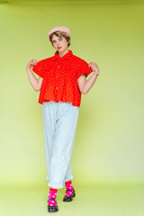 Model wearing Nettle Studios Bleached Floral Chambray Ruffle Pants, a pair of light blue mid-rise wide-leg trousers with an elastic waist and a ruffled hem. Styled in a size-inclusive fashion look against a solid lime green background.