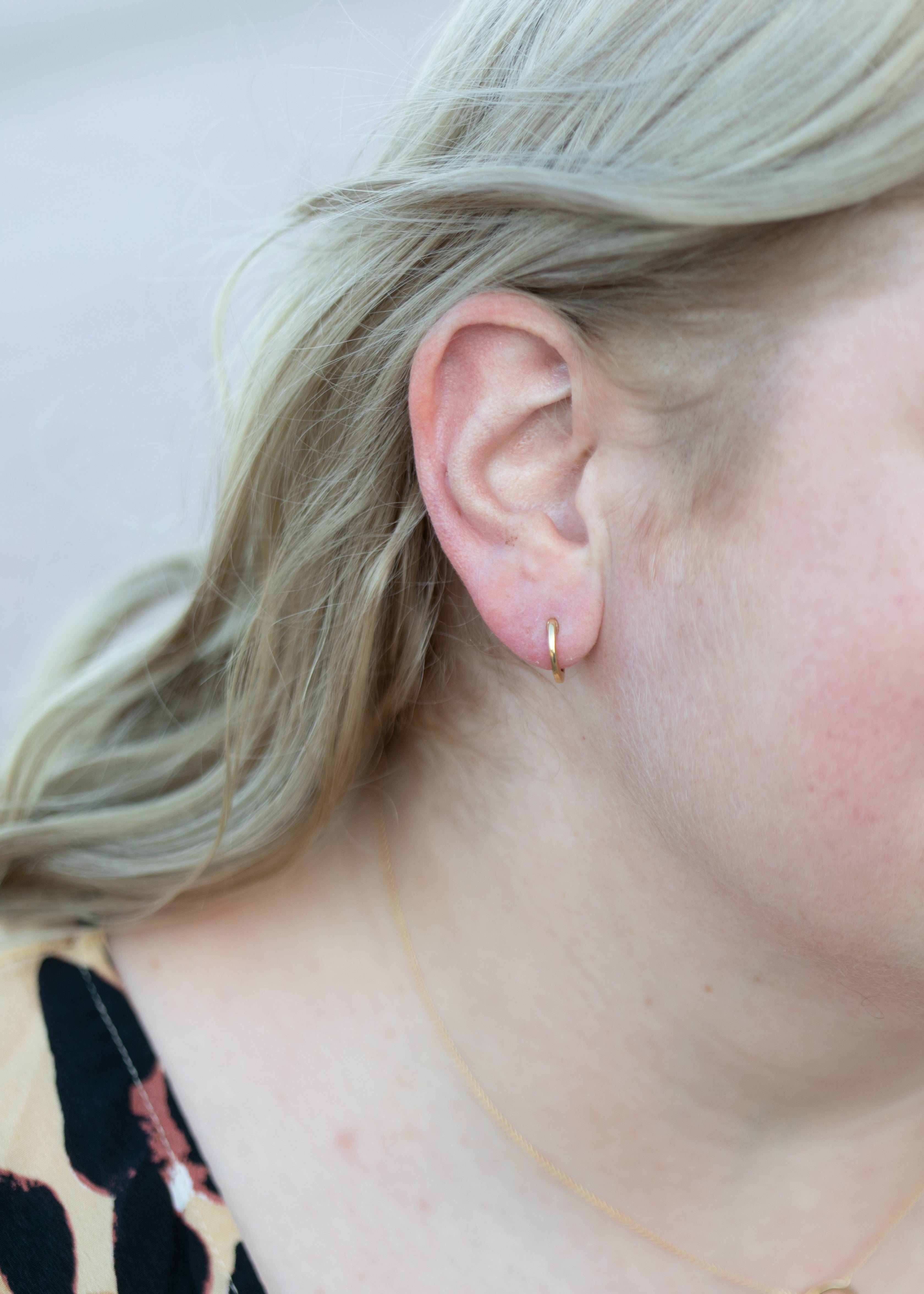 a close up image of a blonde woman's ear with a simple huggie hoop earring in yellow gold. #color_gold