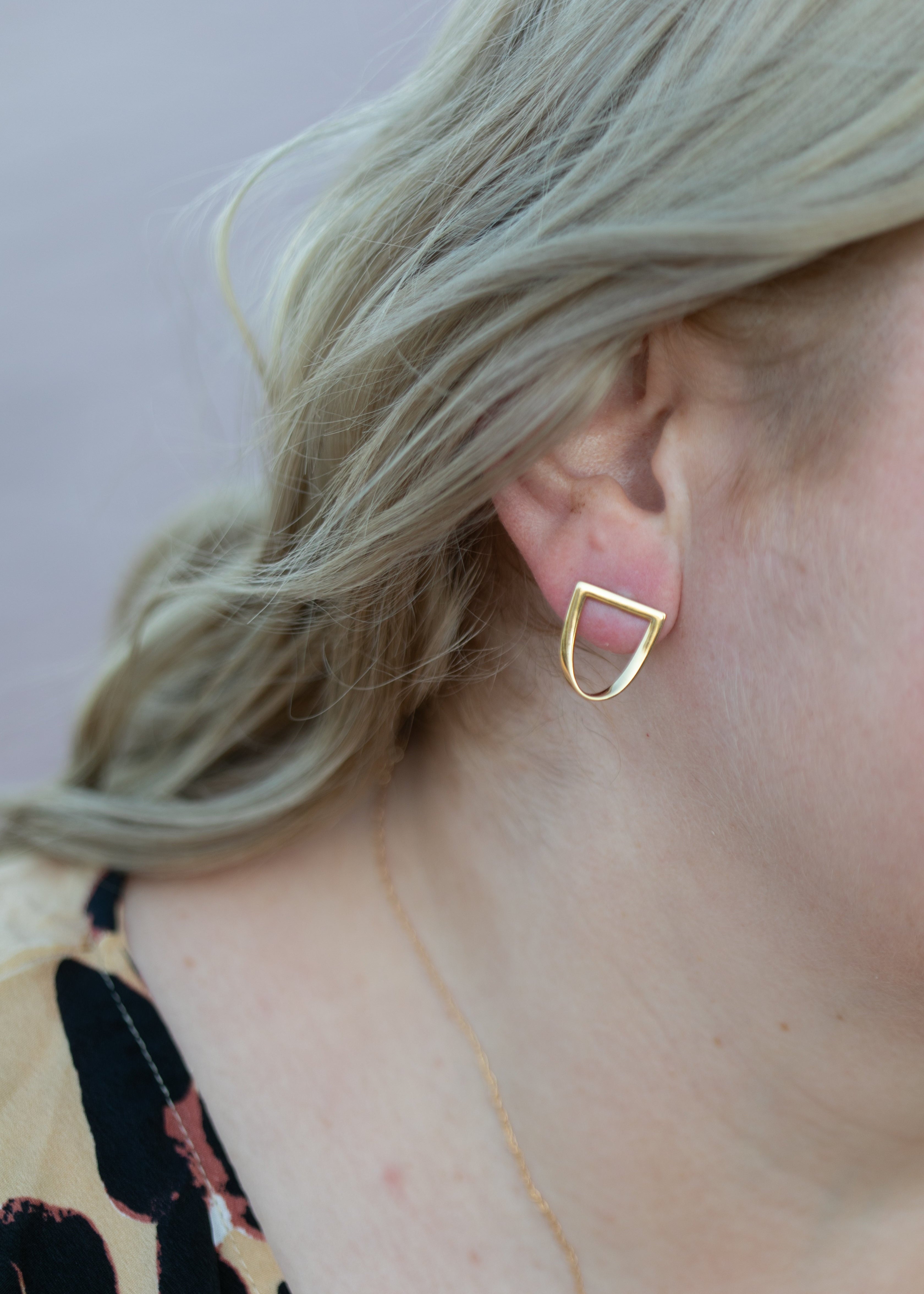 a close up of a blonde wavy haired woman's ear wearing the yellow gold twist earring. #color_gold
