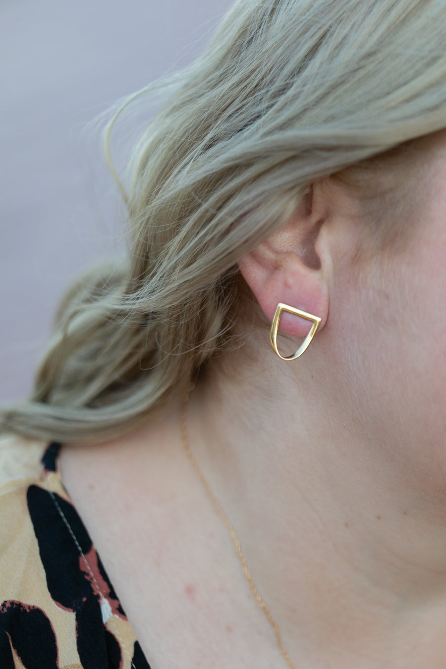 Chouette Designs a close up of a blonde wavy haired woman's ear wearing the yellow gold twist earring
