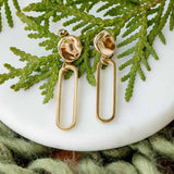 Gold earrings on a white surface with green leaves in the background