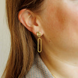 Model wearing the Sela Designs Gold Cleo Earrings, showcasing the 1.5-inch 14k gold-plated oval drop design paired with a plaid blazer.
