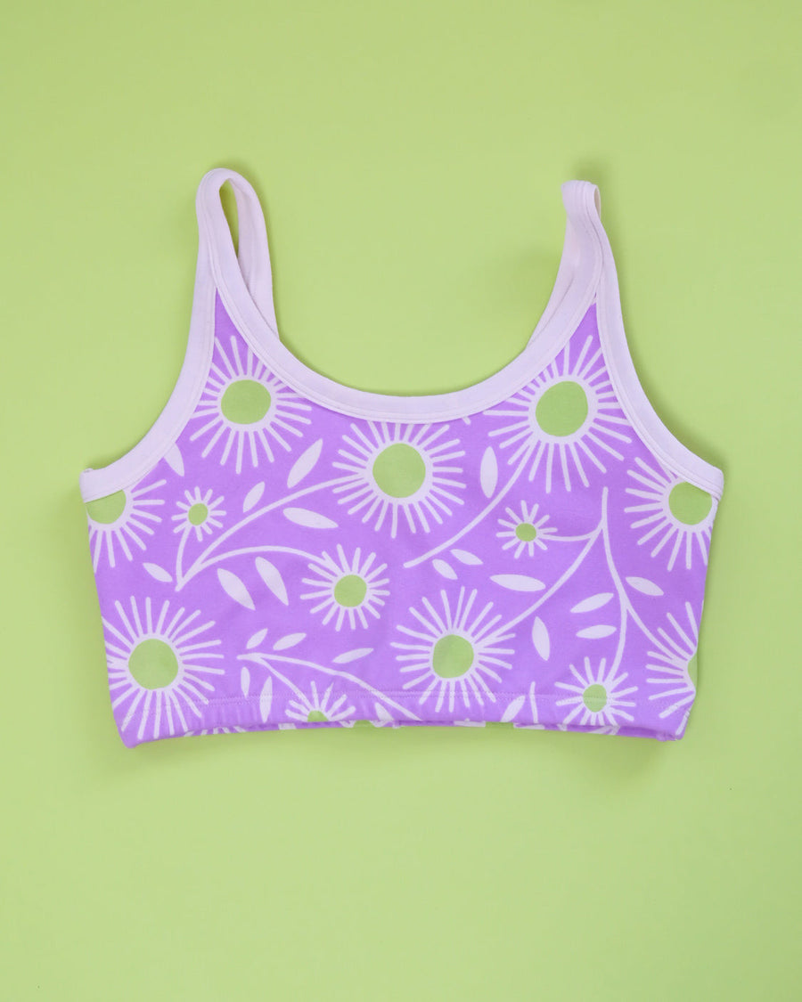 Flat lay product shot showing the back view and scoop neck design of the purple Delia's Daisy longline bra on a green backdrop.