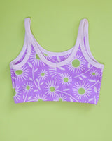 Flat lay product shot showing the front view of the purple Delia's Daisy organic cotton longline bra on a green backdrop.